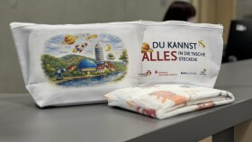 Das Wickelkit: Eine Tasche mit einem Bild auf der Rück- und dem Schriftzug "Du kannst alles in die Tasche stecken" auf einem Tisch, davor liegt eine Windel.